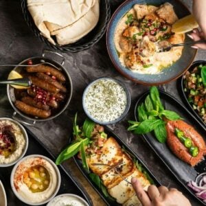 Vibrant spread of Mediterranean-inspired dishes including hummus, grilled halloumi, salads, couscous, and fresh herbs.