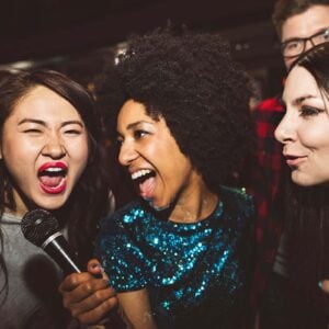 Live karaoke band performing on stage with guests singing along and musicians playing instruments under colorful lights.