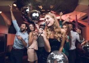 Live karaoke band performing on stage with guests singing along and musicians playing instruments under colorful lights.
