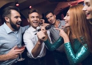 Live karaoke band performing on stage with guests singing along and musicians playing instruments under colorful lights.